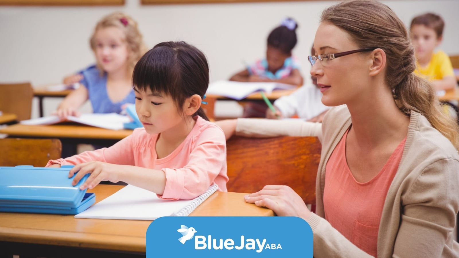 Teacher helping a young student with a learning activity in a classroom during school-based ABA therapy.